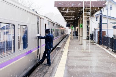 DEC 1, 2018 Hakodate, JAPAN - JR Suoer Hokuto kış aylarında kar yağarken Onuma Koen istasyonunda tren kondüktörü trian kapısında duruyor..