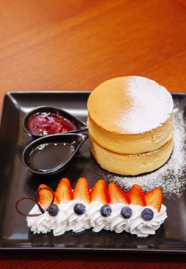 Taze çilekli, yaban mersinli ve siyah tabakta kremalı nefis vişneli pasta.