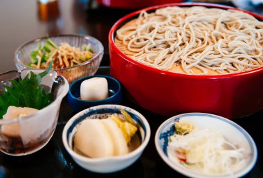 Japon soğuk soba şehriyesi kırmızı bambu tabakta çeşitli mezeler ile. Japon tarzı yemek takımı.