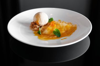 Taze portakal soslu krep pişmiş badem ve siyah masada beyaz tabakta vanilyalı dondurma. Üst görünüm