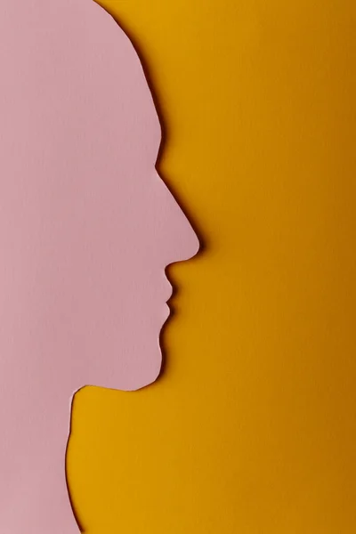 Head silhouette made of paper. Pink paper shaped as a human head with copy space on yellow paper background. Minimal concept.