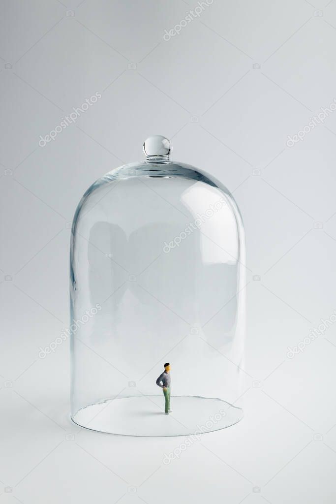 Small figurine in quarantine under a glass dome on a bright background with copy space. Coronavirus prevention, social distancing and Quarantine concept. Self-isolation.