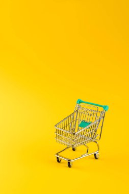 Metalik alışveriş arabası, sarı arka planda fotokopi alanı ile birlikte. Alışveriş sembolü.