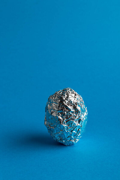 Egg in aluminum foil on blue background with copy space. Easter symbol and sign. One egg.