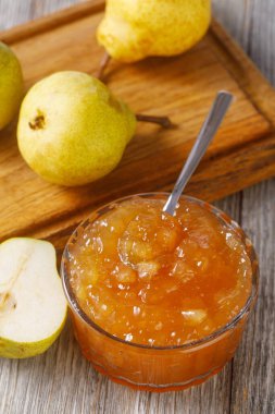 Cam bir kasede armut reçeli, taze armutlarla çevrili.