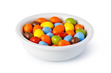 Beyaz arka planda izole edilmiş beyaz bir kaseyi dolduran renkli çikolata şekerleri.