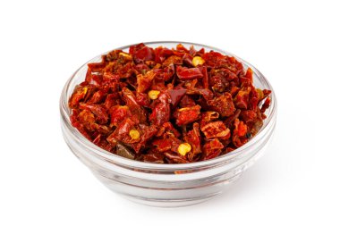 Kırmızı biber taneleri beyaz arka planda cam bir kaseyi dolduruyor.