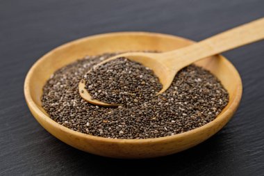Ahşap bir kaseyi koyu bir arka planda kaşıkla dolduran Chia tohumları
