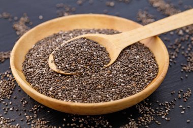 Ahşap bir kaseyi koyu bir arka planda kaşıkla dolduran Chia tohumları