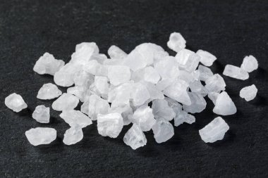 Kaba deniz tuzu kristalleri koyu arkaplanda bir yığın halinde dizilir.