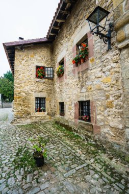 SANTILLANA DEL MAR, CANTABRIA, SPAIN - 31 Ağustos 2016: Saksılarda bitkilerle süslenmiş çok sayıda pencereli eski taş bina