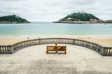 SAN SEBASTIAN, İspanya - 30 Ağustos 2016: Kürsüde oturan ve San Sebastian Concha plajının deniz manzarasını izleyen üç yetişkin turistin geçmişi.