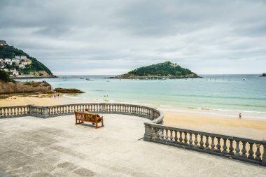 SAN SEBASTIAN, İspanya - 30 Ağustos 2016: Kürsüde oturan ve San Sebastian Concha plajının deniz manzarasını izleyen üç yetişkin turistin geçmişi.