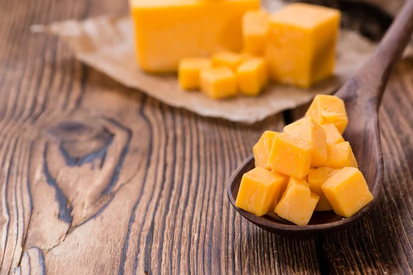 Pieces of Cheddar (detailed close-up shot) on rustic wooden background — Stock Photo, Image