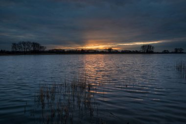 Sessiz bir gölün üzerinde gün batımı ve akşamları karanlık bulutlar, bahar manzarası.