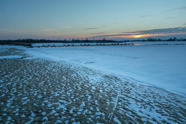 Sandy beach covered with snow and sunset over a frozen lake, Zoltance, Lubelskie, Poland