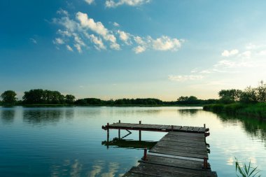 Ahşap bir balıkçı iskelesi ve sakin mavi bir göl.