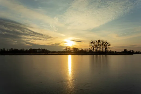 Pôr do sol sobre um lago congelado com árvores na costa — Fotografia de Stock