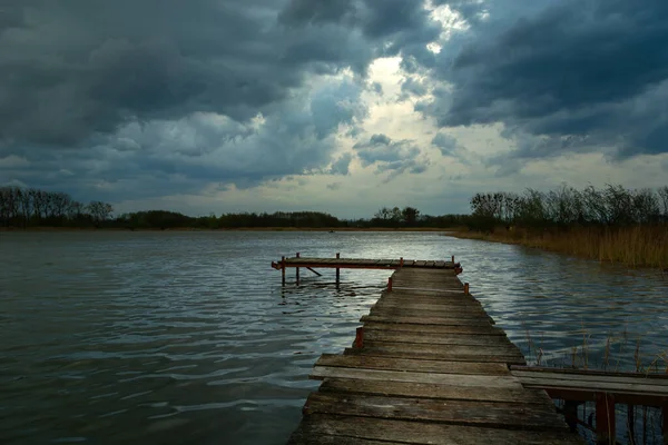 Cais de madeira em um lago e nuvens escuras no céu — Fotografia de Stock