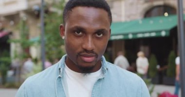 İyi görünümlü, kendine güveni olan, modern, sakallı, siyah derili, küpeli, eski şehrin yakınlarındaki bir kafede kameraya bakan bir adamı yakından çek.