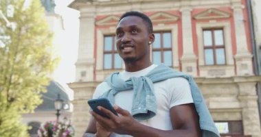 Güzel görünüşlü, gülümseyen, modern Afrikalı, sakallı bir Amerikalının portresi. Sokakta eski mimari ve daktilo ile duruyor.
