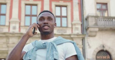 Yakışıklı, neşeli, siyah tenli, sıradan elbiseli bir genç. Eski şehir binalarının yanında duruyor ve yaz günü olumlu bir telefon görüşmesi yapıyor.