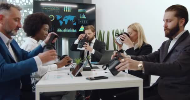 Jóképű, magabiztos, többnemzetiségű, felnőtt irodai munkatársak, akik virtuális valóság headsetet viselnek a tanácsteremben végzett közös munka során. — Stock videók