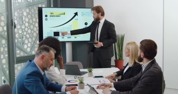 Zakelijk concept waar knappe positieve bebaarde teamleider een presentatie houdt op digitaal whiteboard in vergaderruimte voor geconcentreerde collega 's van gemengde rassen — Stockvideo