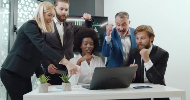 Хорошо выглядящие успешные успешные бизнесмены получают хорошие новости на экране ноутбука и празднуют победу с поднятыми руками — стоковое видео