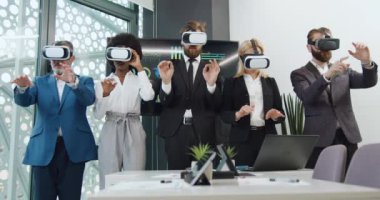 Modern ofis odasındaki kameranın önünde hayali ekranda çalışan, sanal gerçeklik kulaklığı takmış özgüvenli, çok kültürlü beş şirket çalışanının portresi.