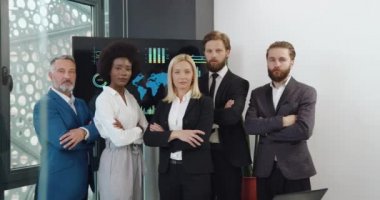 Modern toplantı odasında kollarını kavuşturmuş kameranın önünde duran iyi görünümlü, konsantre olmuş başarılı uluslararası işçi takımının ön görüntüsü.