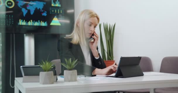 Крупный план привлекательной уверенной высококвалифицированной успешной предпринимательницы, которая разговаривает по телефону и одновременно работает на i-pad — стоковое видео