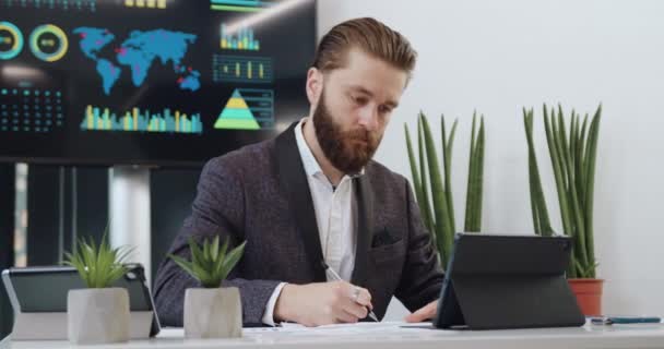 Sannolikt självsäker seriös erfaren hårt arbetande vuxen skäggig kontorschef som arbetar på tablet pc i sitt kontorsrum — Stockvideo
