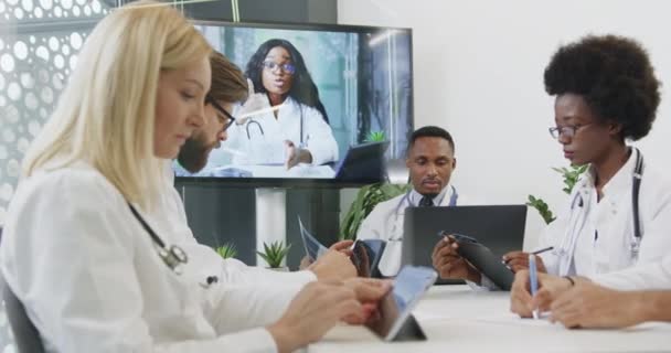 Concept de médecine où les personnes médicales multiethniques expérimentées et confiantes ayant une réunion vidéo en ligne avec une collègue conjointe à la peau noire dans une salle de réunion — Video