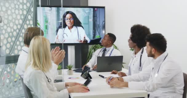 Portrait of good-looking confident experienced mixed race medical people which having video call with their black-skinned colleague and clapping hands after her speech — Stock Video