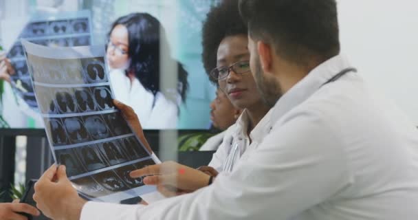 Dos personas médicas experimentadas y confiadas que analizan la radiografía de los pacientes durante la reunión en la sala de oficina con otros miembros del equipo — Vídeo de stock