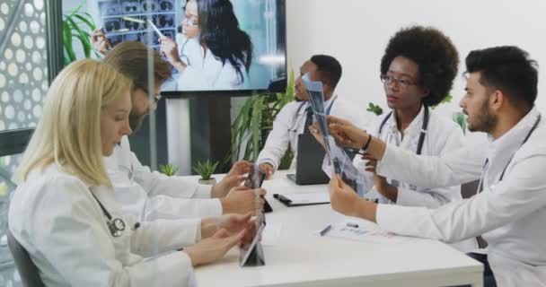 Equipe médica de sucesso altamente qualificada de boa aparência que revisa a varredura de raios X dos pacientes e aconselha sobre o tratamento com outros membros e médico chefe feminino através de videochamada — Vídeo de Stock