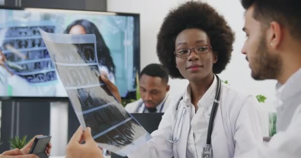 两位不同种族的医生在与医生个人的联席会议上讨论病人的X光并决定治疗方法，这是有可能达到的专业目的 — 图库视频影像