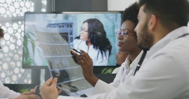 Ritratto di simpatici e fiduciosi colleghi medici internazionali altamente qualificati che discutono l'istotia della revisione della radiografia del paziente e decidono il metodo di trattamento — Video Stock