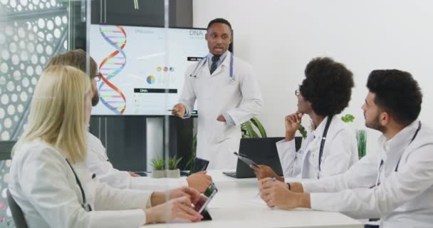 Привлекательный опытный чернокожий врач, стоящий рядом с интерактивным экраном и представляющий доклад о внутренних человеческих органах перед международными медицинскими коллегами — стоковое видео