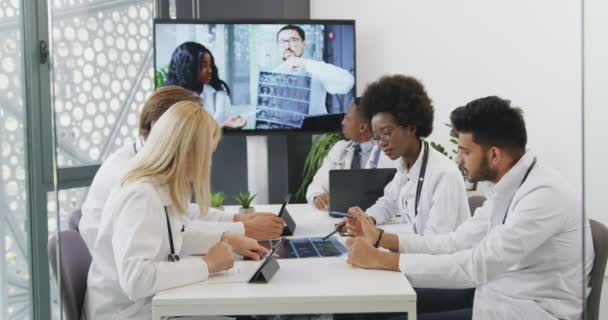 Attraente fiducioso sperimentato successo misto razza persone mediche che hanno videoconferenza con il loro partner sul monitor digitale durante la riunione congiunta — Video Stock
