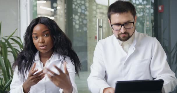 Z przodu widok dwóch wysoko wykwalifikowanych ufnych międzynarodowych kolegów medycznych, którzy organizują konferencję online dla swoich partnerów lub nagrywanie webinarium przed kamerą — Wideo stockowe