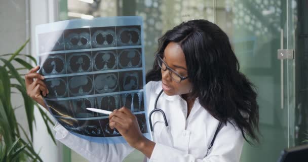 온라인 비디오 콘퍼런스에서 동료들에게 X-ray 이미지를 보여 주는 믿을 만 한 경험이 많은 흑인 피부의 여의사의 사진을 클로즈업 한 사진. — 비디오
