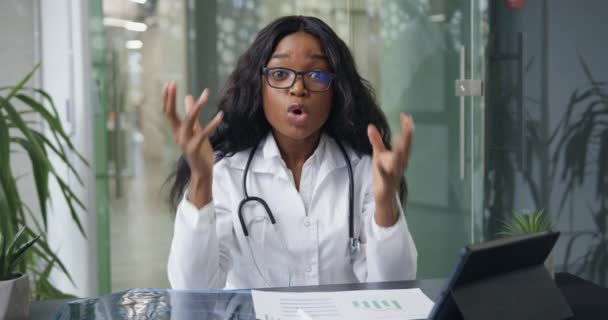 Insatisfecha confiada experimentada trabajadora médica de piel negra explicando emocionalmente los métodos de tratamiento durante la videoconferencia en línea, cámara lenta — Vídeos de Stock