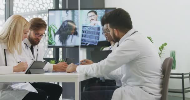 Beau confiant multiracial réussi médecins masculins et féminins travaillant ensemble dans la salle de conférence en ligne avec leurs partenaires médicaux — Video