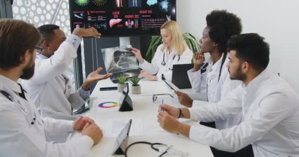 Медицинская концепция, в которой уверенная высококвалифицированная, привлекательная международная команда врачей обсуждает возможности рентгеновского изображения пациентов и подбирает методы лечения — стоковое видео