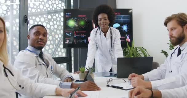 Aantrekkelijke glimlachende gewaardeerde succesvolle gemengde ras artsen poseren op camera met duimen omhoog tijdens de vergadering in de vergaderzaal — Stockvideo