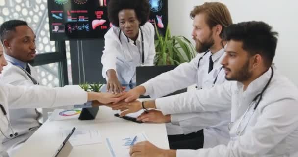 Aantrekkelijke positieve gelukkige hoogopgeleide multi-etnische mannelijke en vrouwelijke medische collega 's die de handen ineenslaan als een teken van goed partnerschap en vertrouwen — Stockvideo