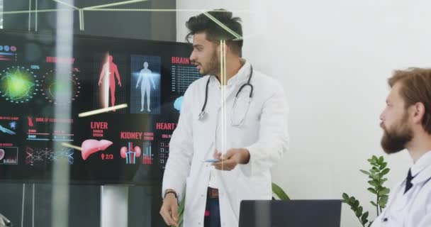 Medizinisches Konzept, wo attraktive selbstbewusste erfahrene bärtige medizinische Fachangestellte eine Präsentation auf interaktivem Monitor über Risiken Herzkrankheit Thema vor anderen Kollegen halten — Stockvideo