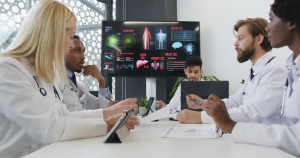 De beaux médecins de race mixte expérimentés et positifs conseillent sur les risques de maladies cardiaques lors d'un briefing en salle de conférence, vue de face — Video